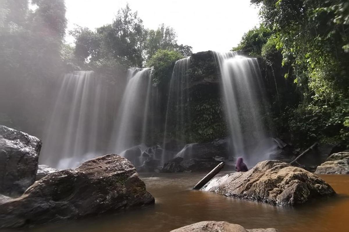 a waterfall with a person sitting in front of it