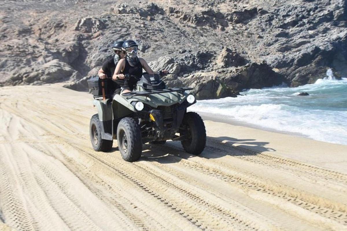 Dos personas montando un quad en la playa