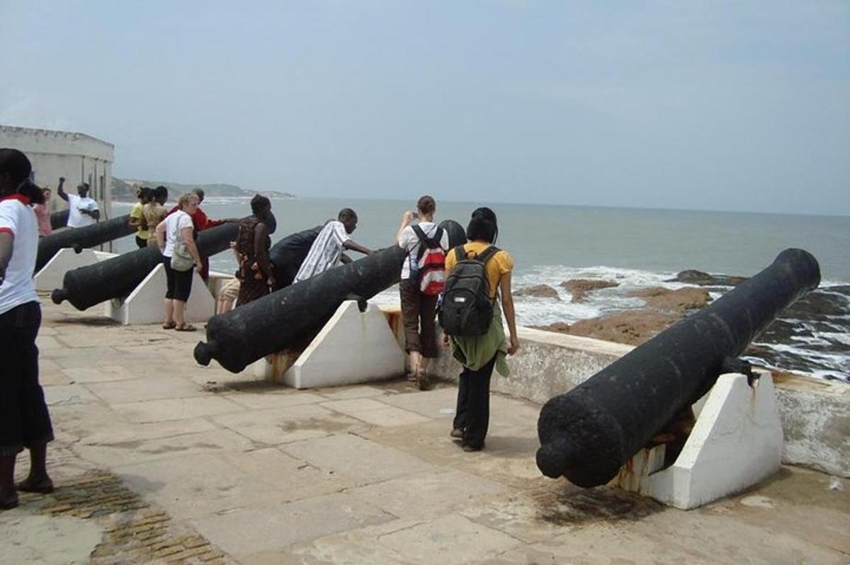 a group of people standing near the ocean with cannonballs