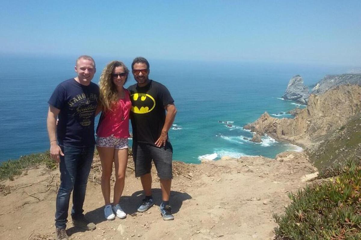 tre persone in piedi in cima a una scogliera vicino all'oceano