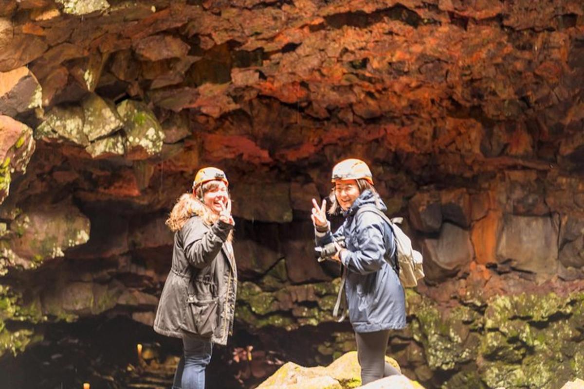 zwei Menschen stehen auf Felsen vor einer Höhle