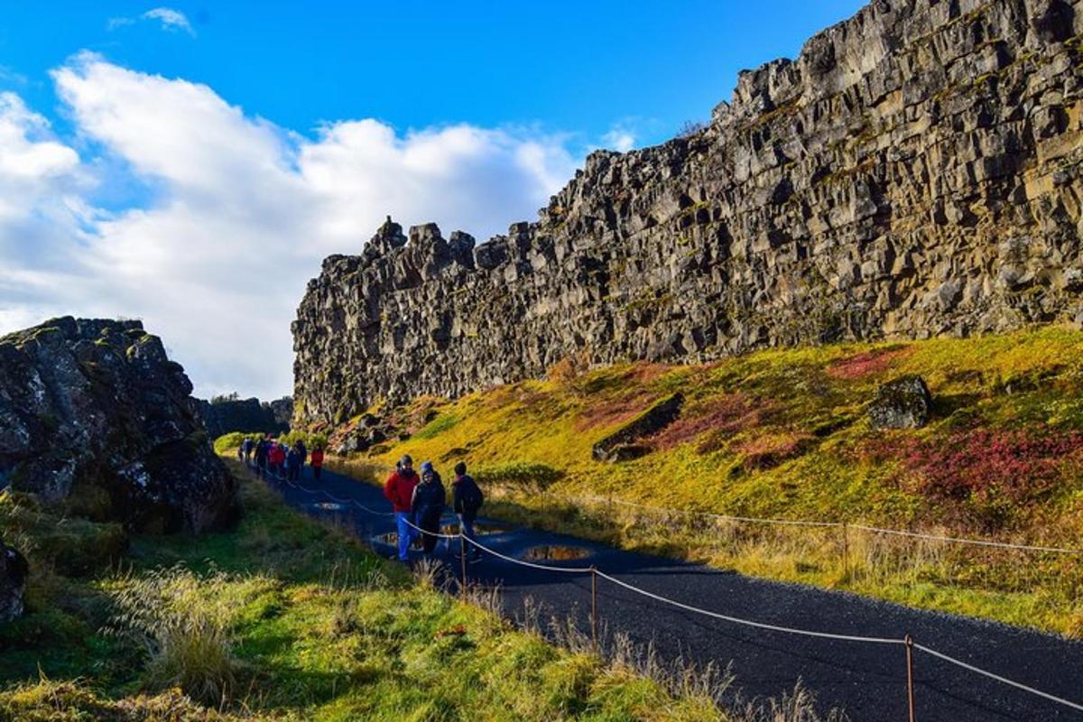 um grupo de pessoas caminhando por uma estrada ao lado de um muro de pedra