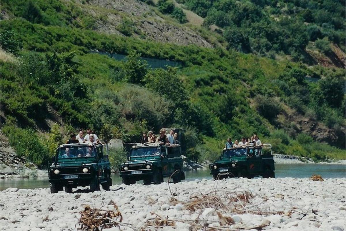 eine Gruppe von Menschen, die auf der Ladefläche von drei Jeeps in einem Fluss fahren