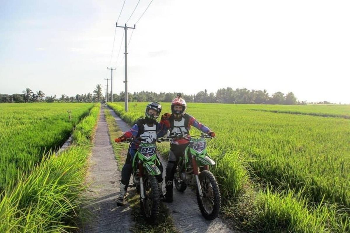 two people riding motorcycles on a dirt road in a field