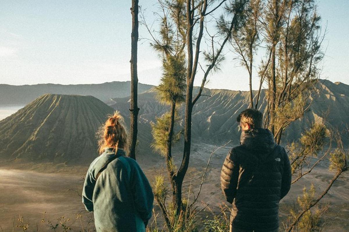 two people standing on a hill looking out at the mountains
