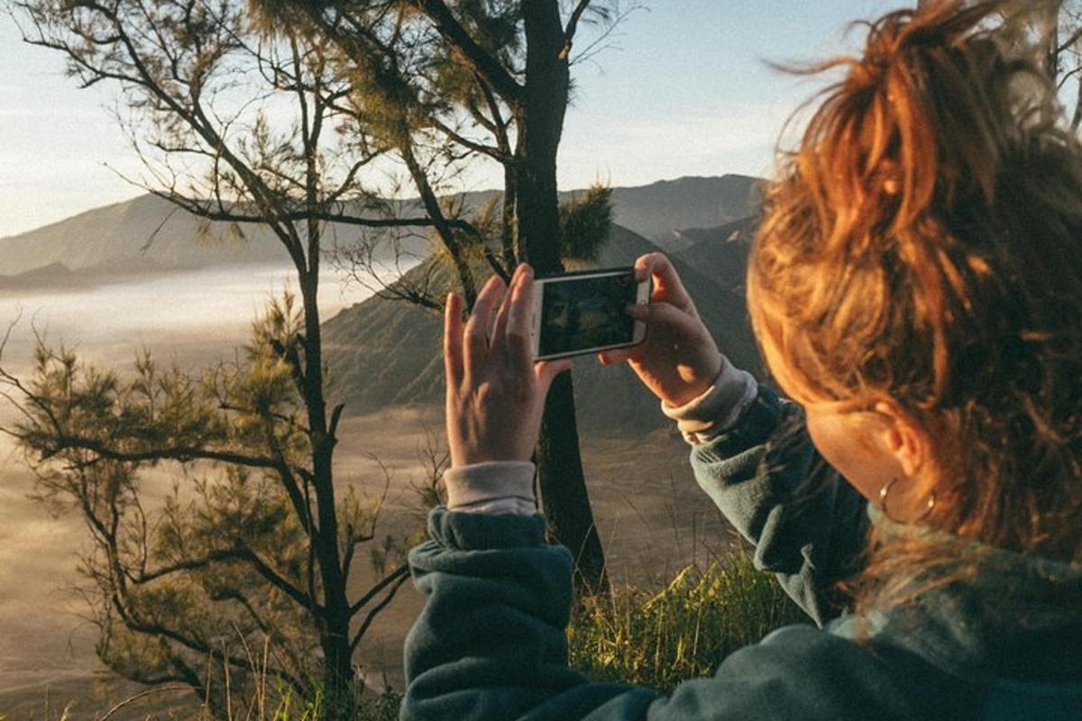a woman taking a picture of the mountains with her cell phone