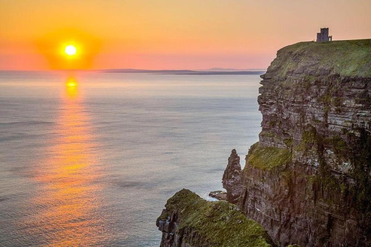 a sunset over the ocean with a lighthouse on a cliff