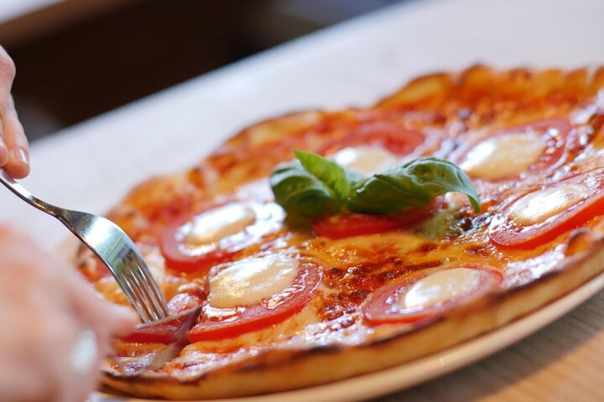 osoba krájející pizzu vidličkou a nožem