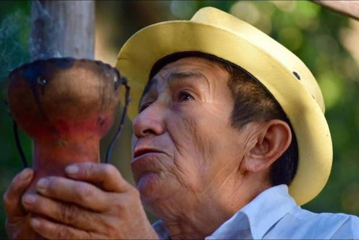 un uomo anziano che indossa un cappello e tiene in mano un oggetto di legno