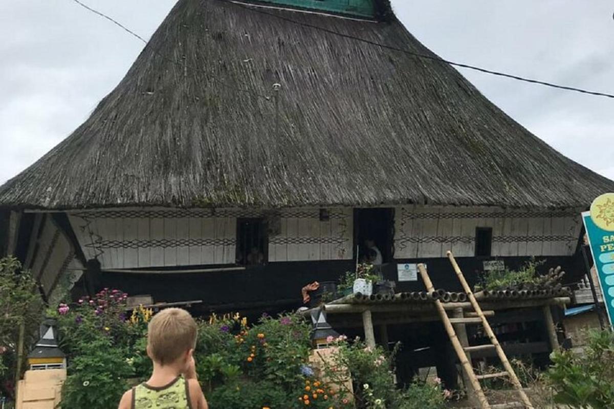 Ungur drengur stendur fyrir framan stráþakað hús