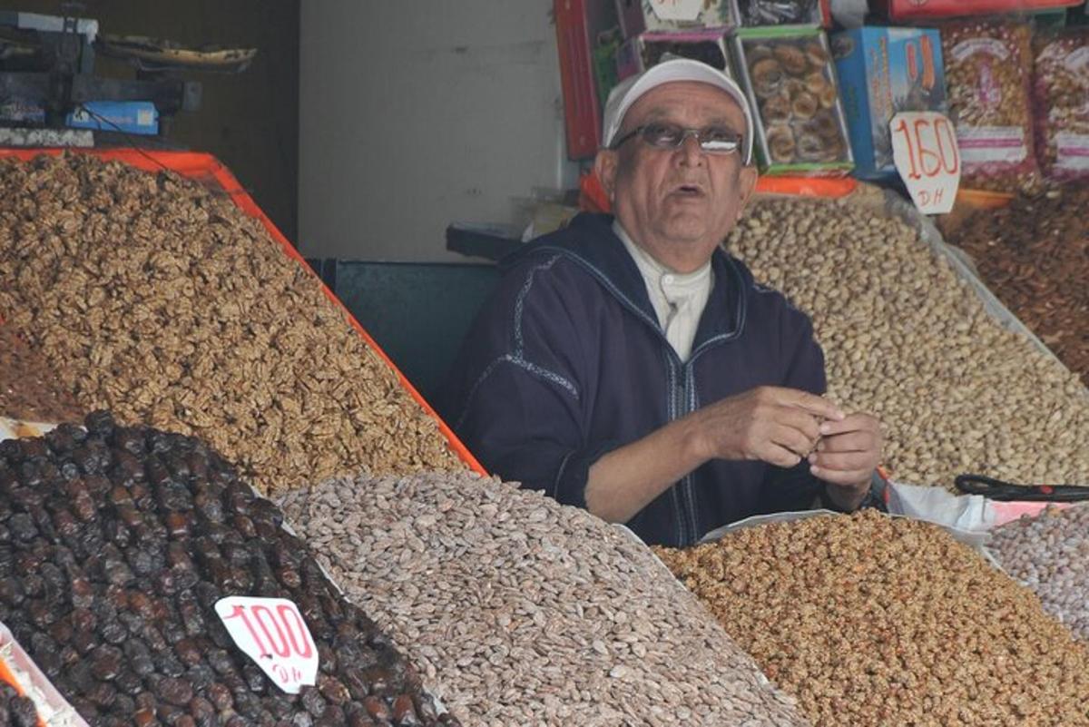 muž sedící na trhu s hromadou ořechů