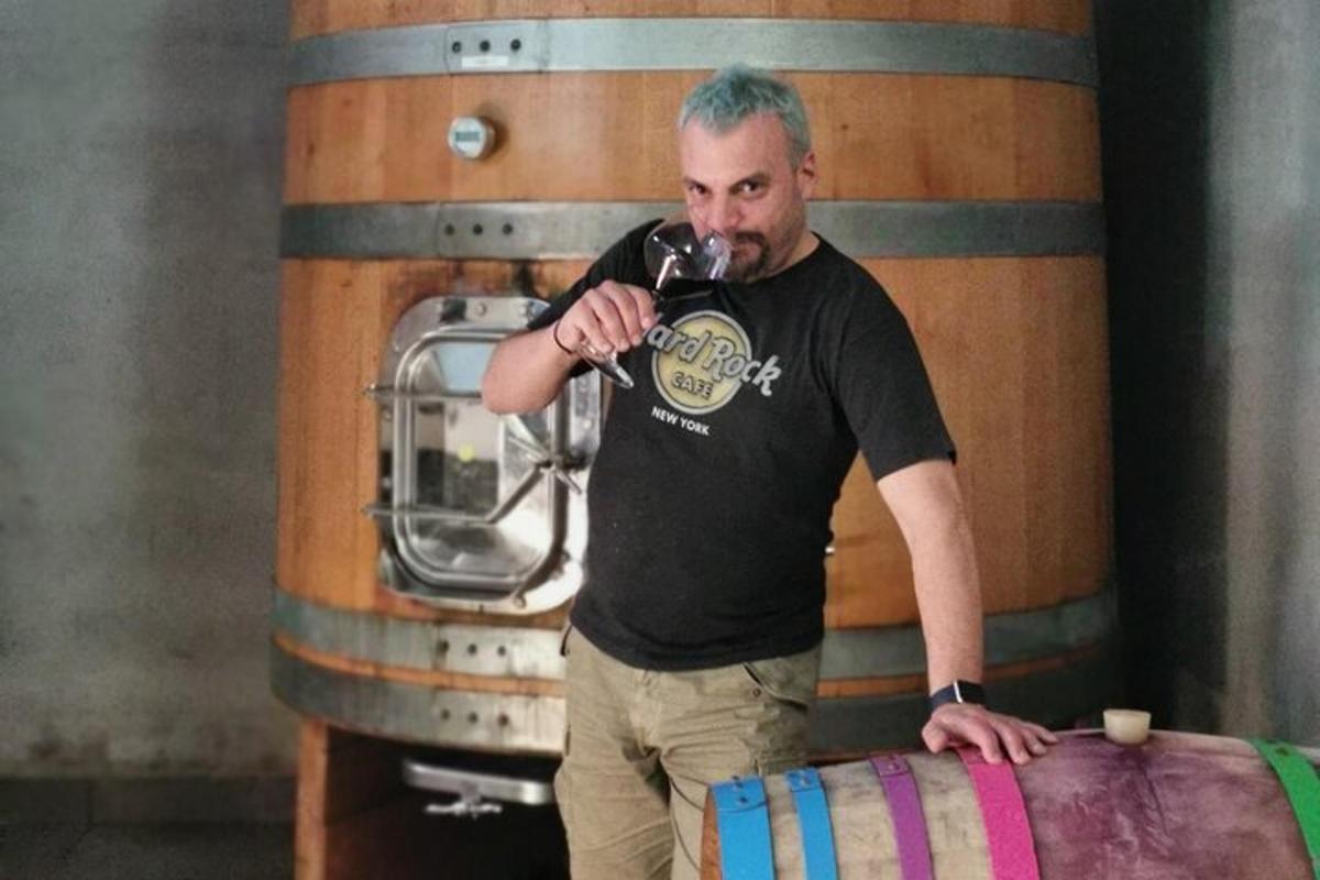 a man drinking a glass of wine next to a barrel