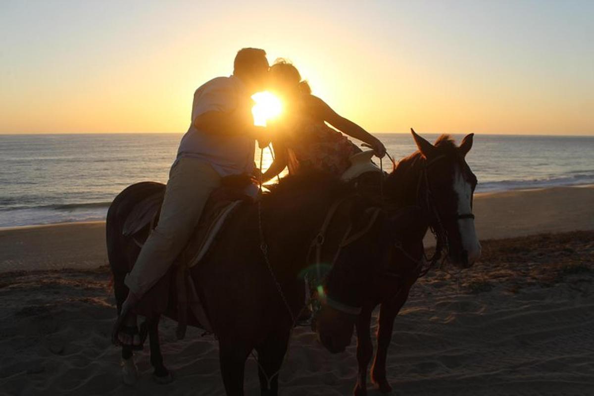 due persone a cavallo sulla spiaggia al tramonto