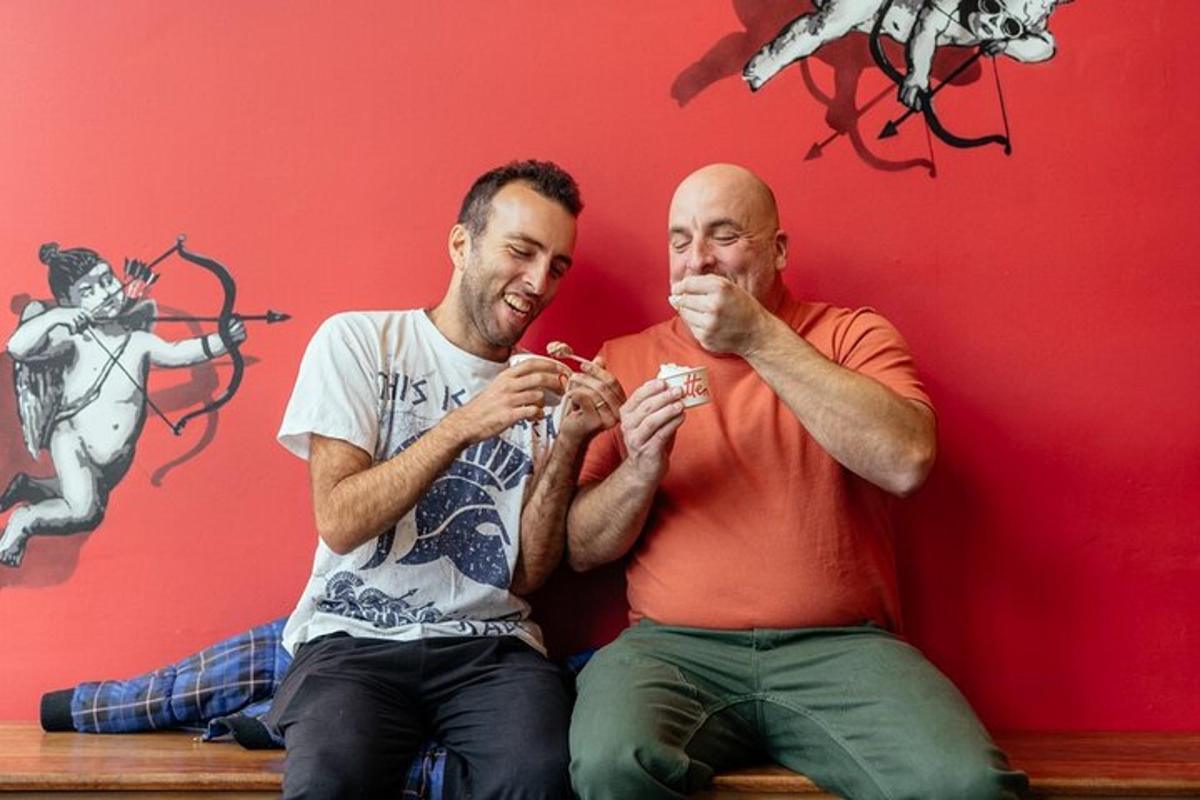 two men sitting on a bench eating food
