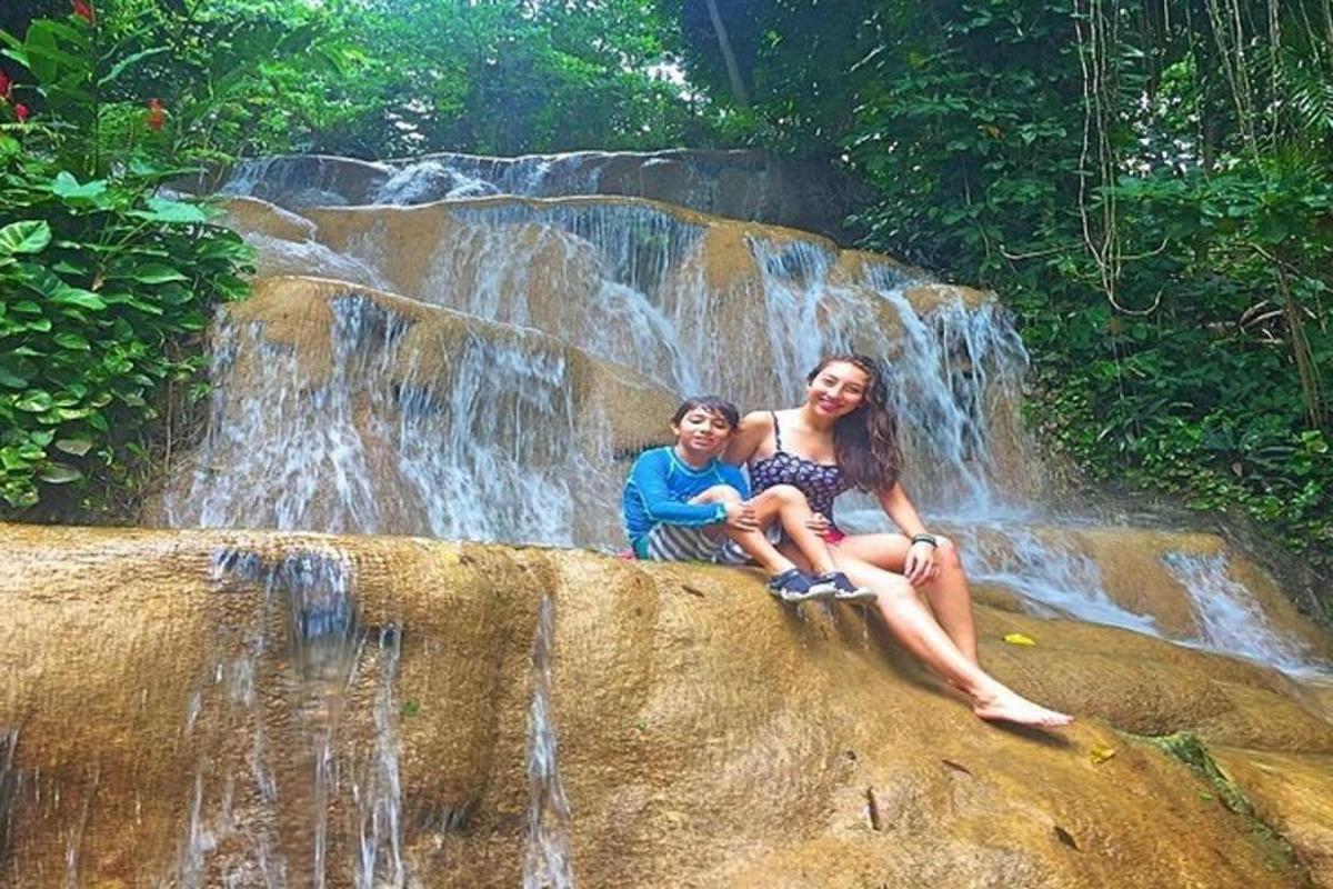 uma mulher e uma criança sentadas em uma rocha em frente a uma cachoeira