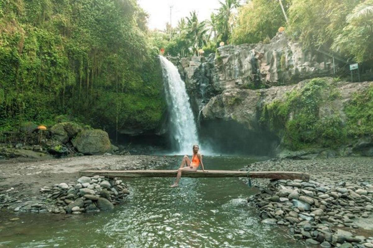 a woman sitting in the water in front of a waterfall