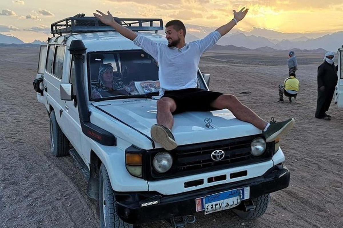 muž sedící na kapotě auta v poušti