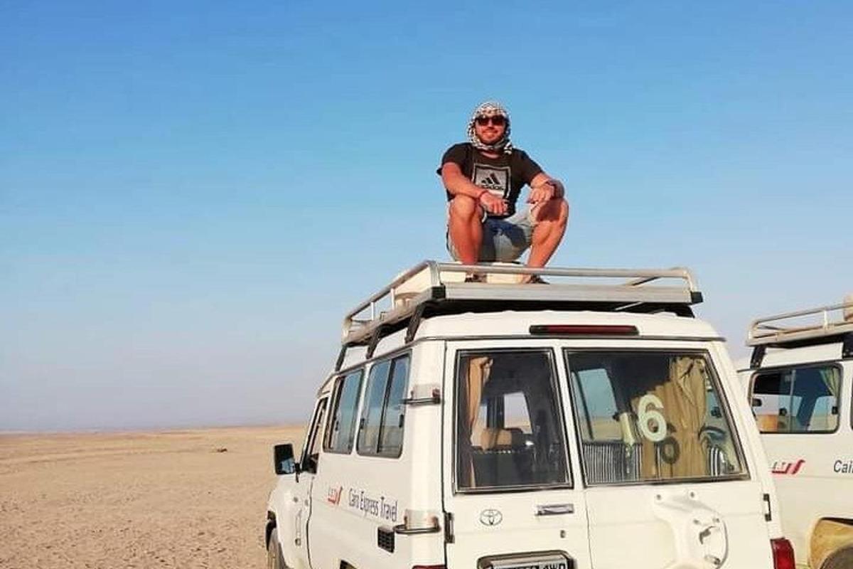 Un hombre sentado en el techo de una camioneta blanca en el desierto.