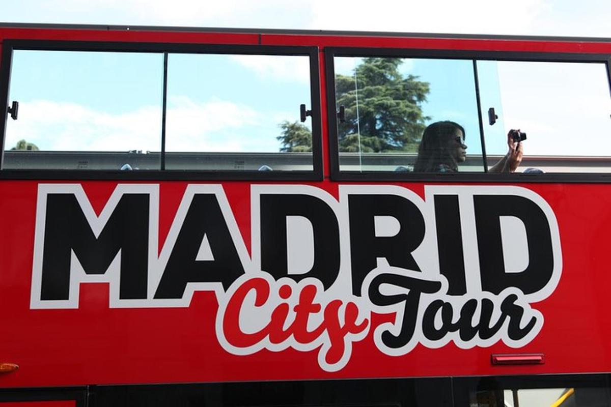 a person taking a picture of the side of a red bus