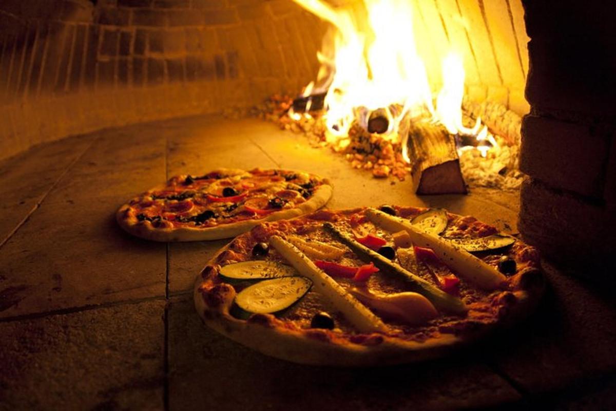 dvě pizzy sedící v cihlové peci