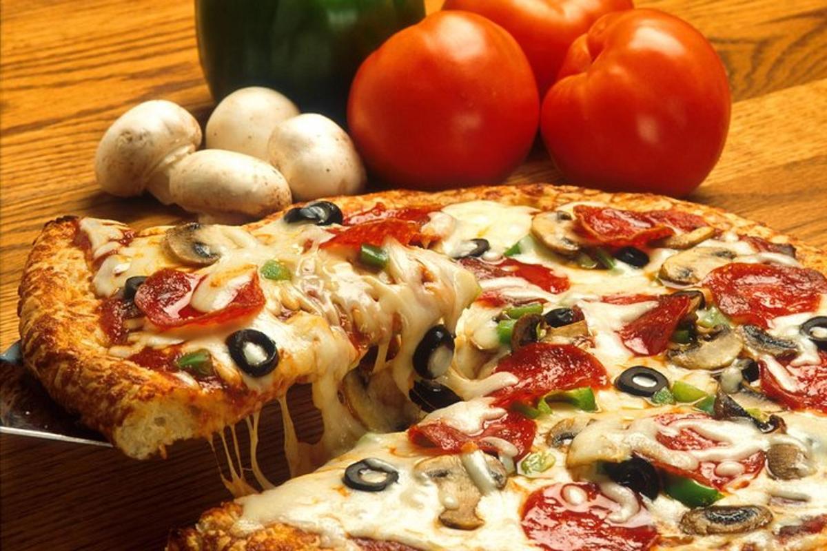 kousek pizzy na stole s rajčaty a houbami