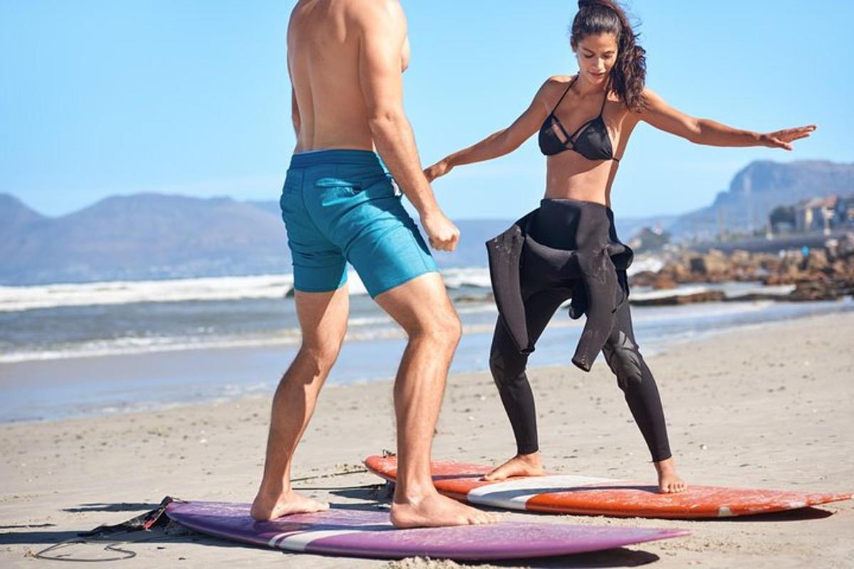 Un hombre y una mujer de pie sobre tablas de surf en la playa
