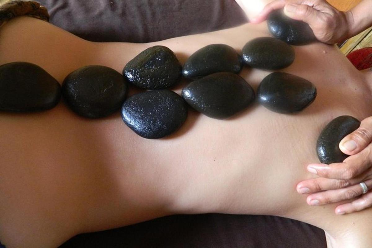 una donna che si tiene la schiena con delle pietre nere sulla schiena