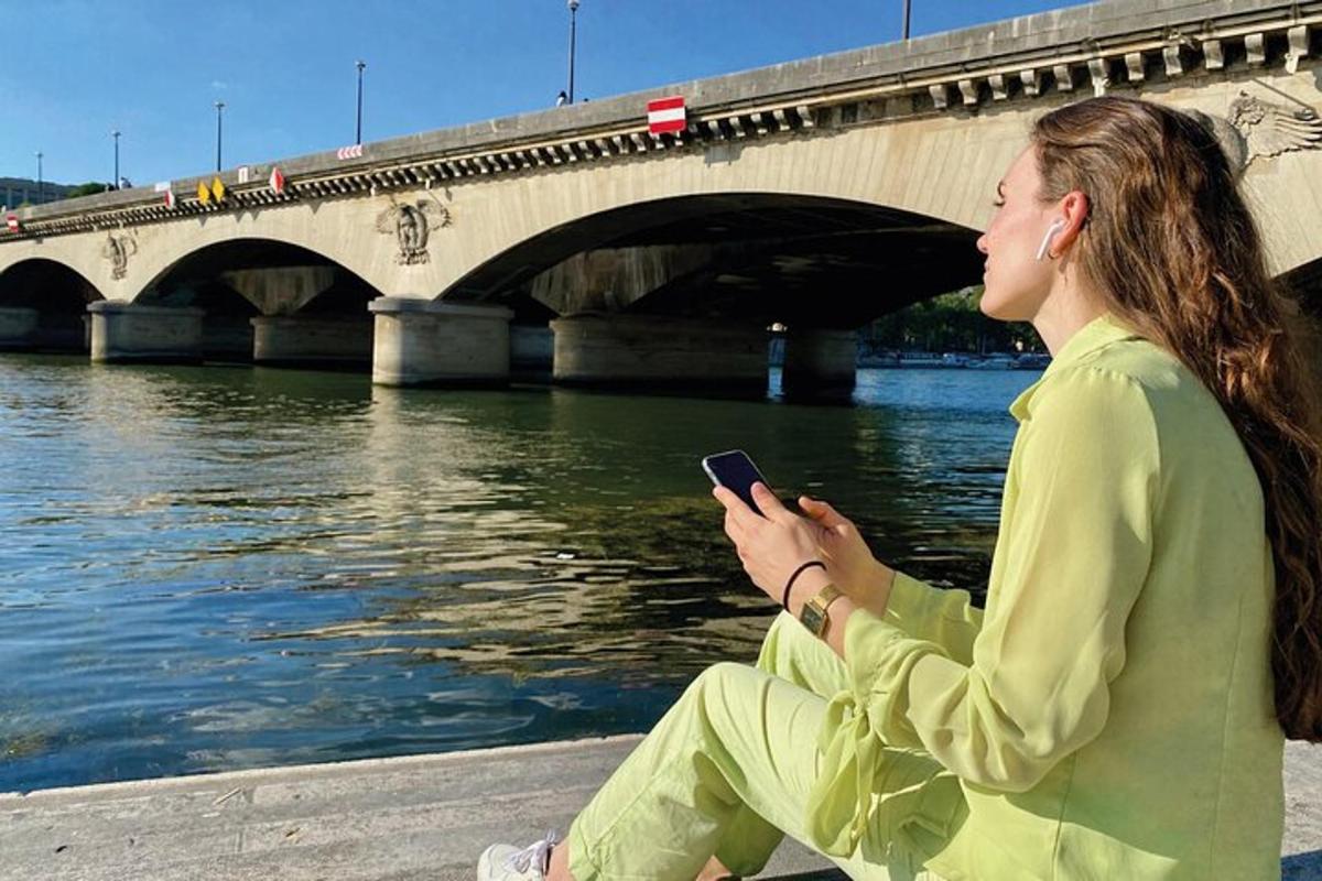 una donna seduta vicino a un fiume che guarda un cellulare