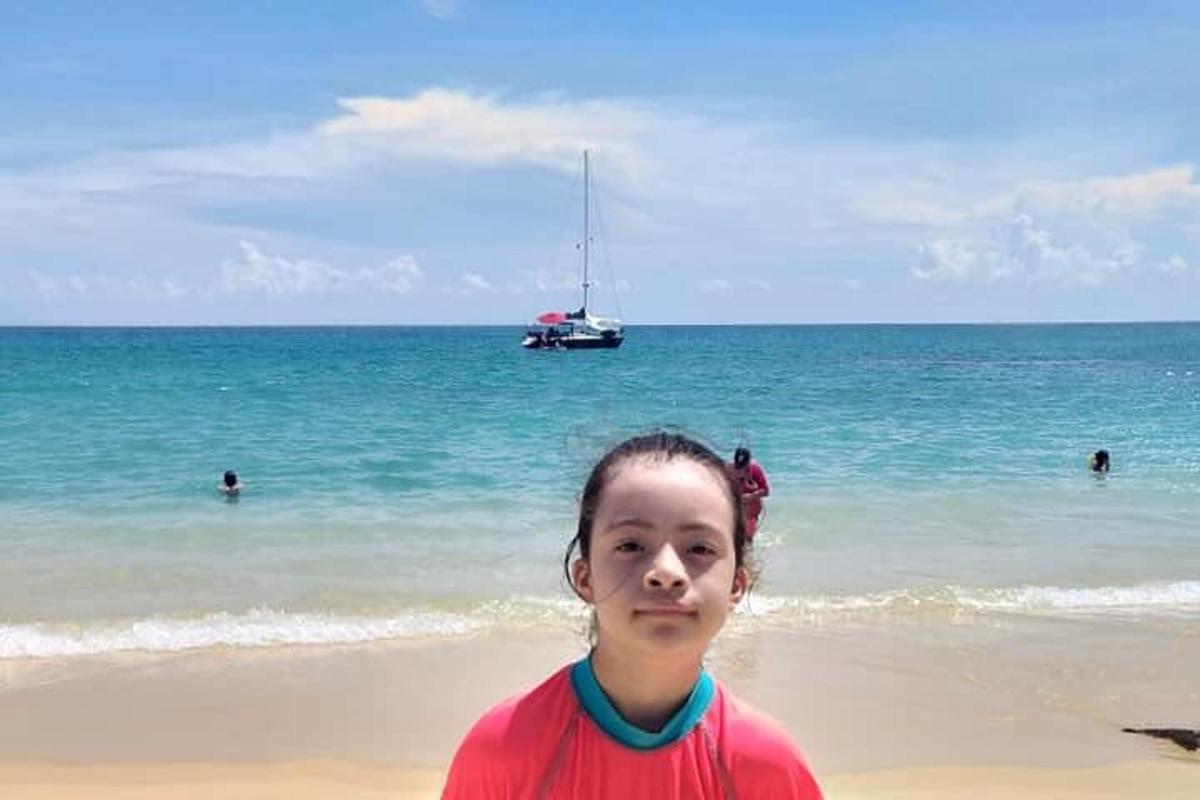 una bambina in piedi sulla spiaggia con una barca nell'oceano