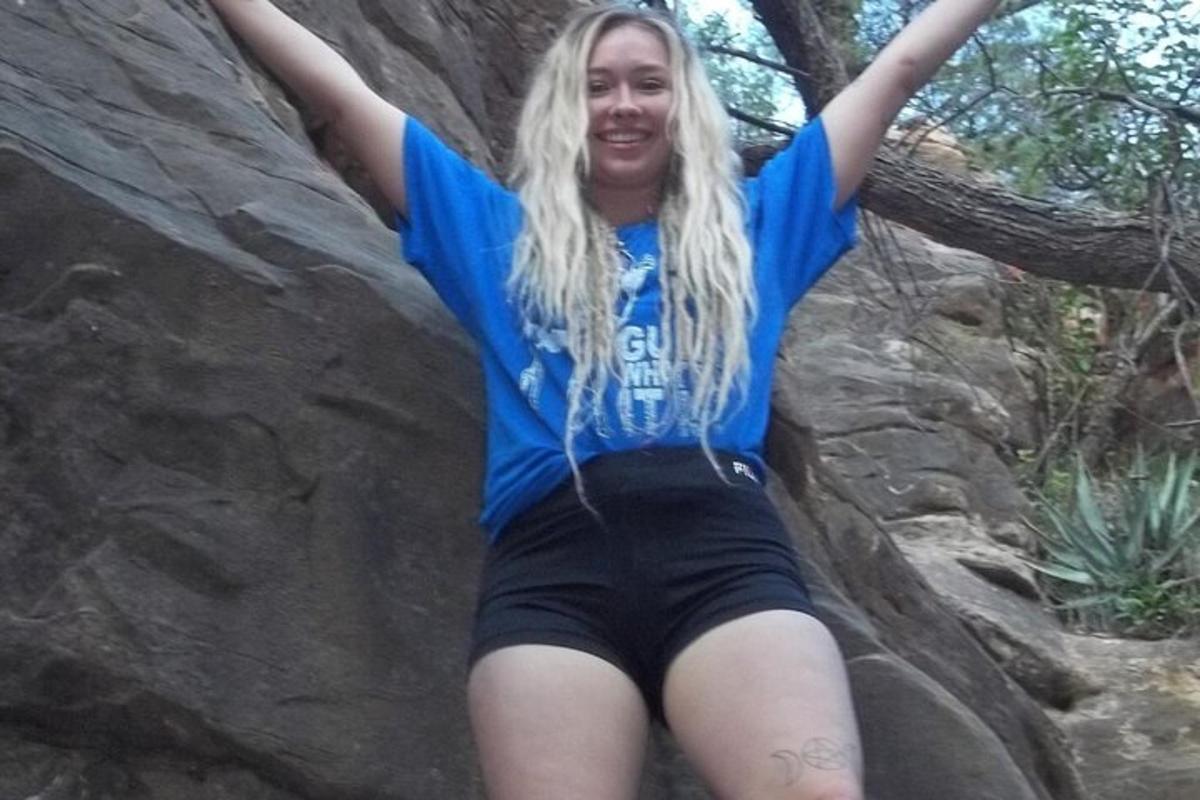 uma mulher sentada em uma rocha com os braços no ar