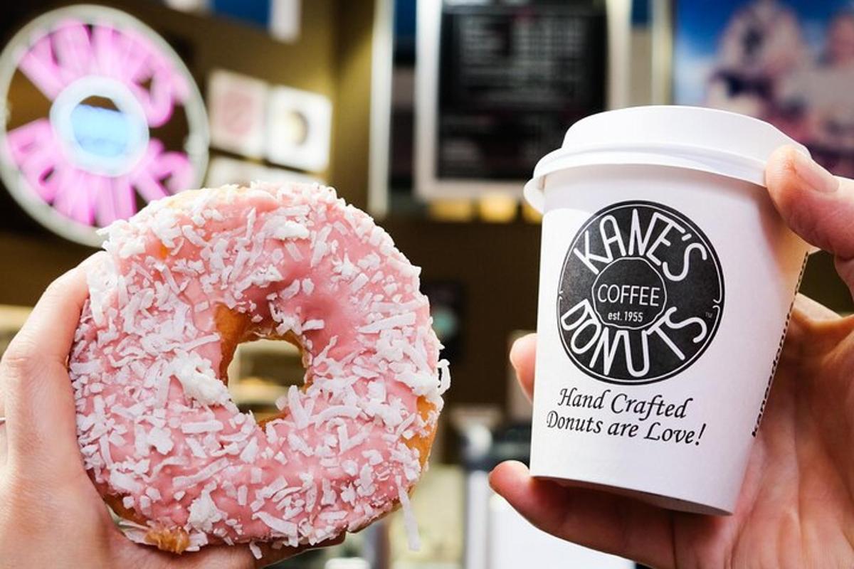 uma pessoa segurando um donut rosa e uma xícara de café