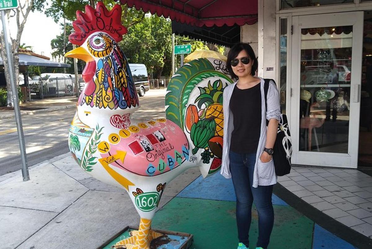 seorang wanita berdiri di sebelah patung besar seekor ayam