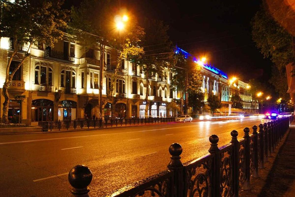 a city street at night with a fence and buildings