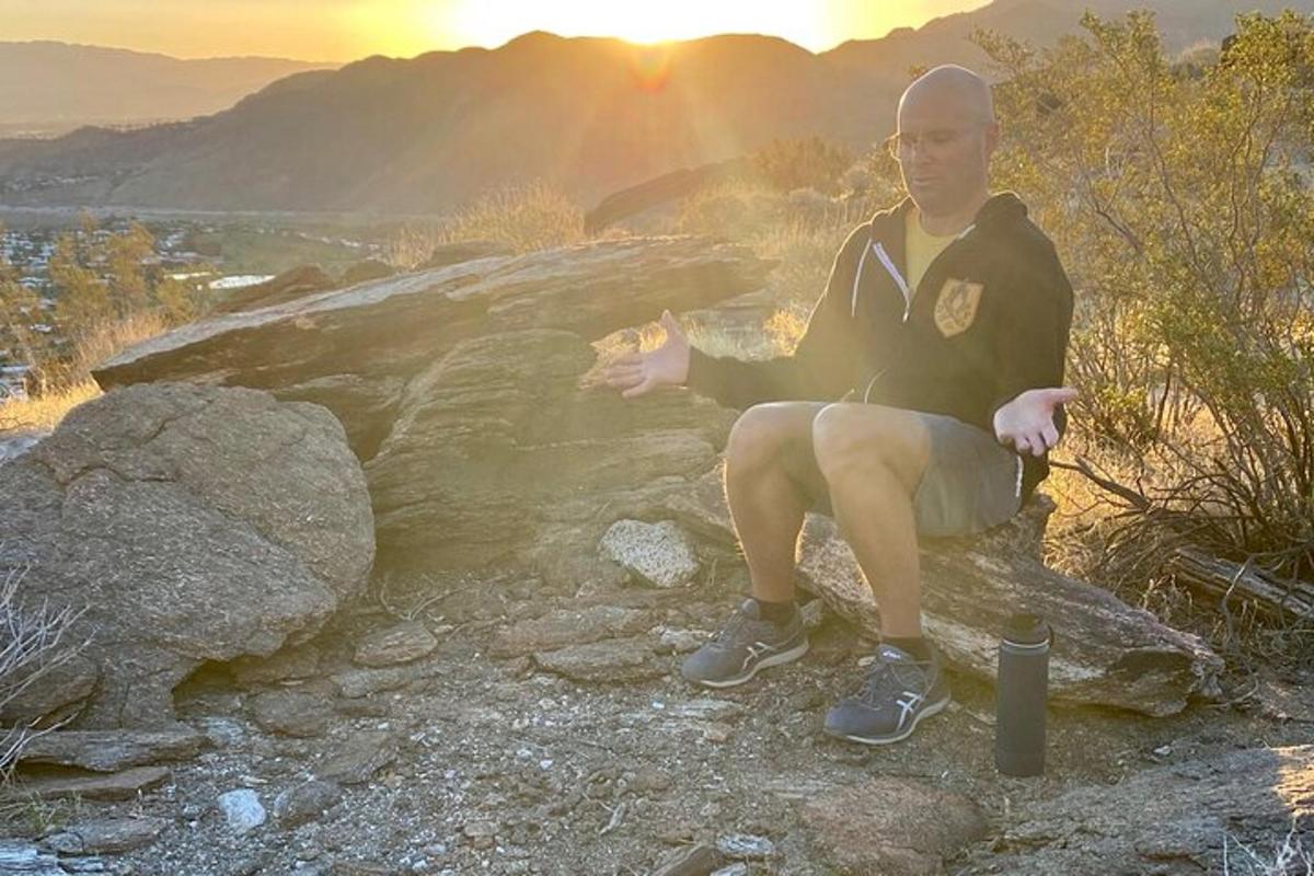 en man som sitter på en sten med solnedgången i bakgrunden
