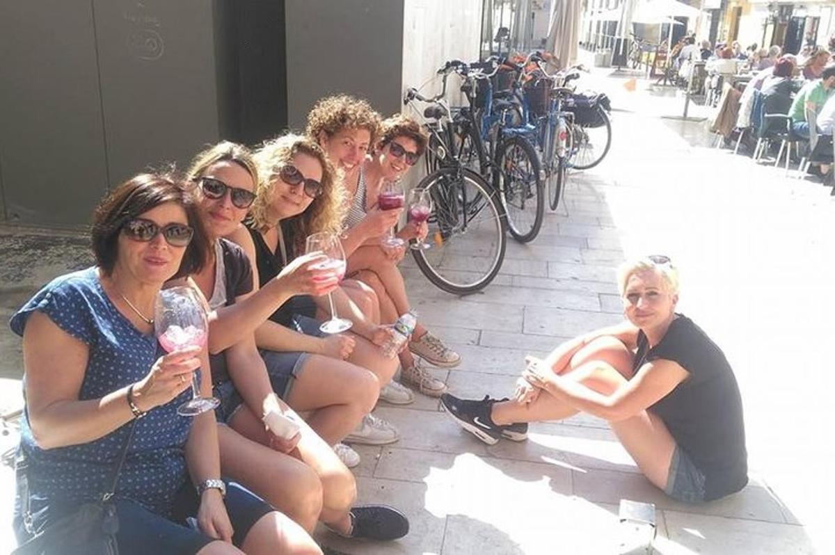 grupa žena koje sjede na tlu držeći čaše za vino