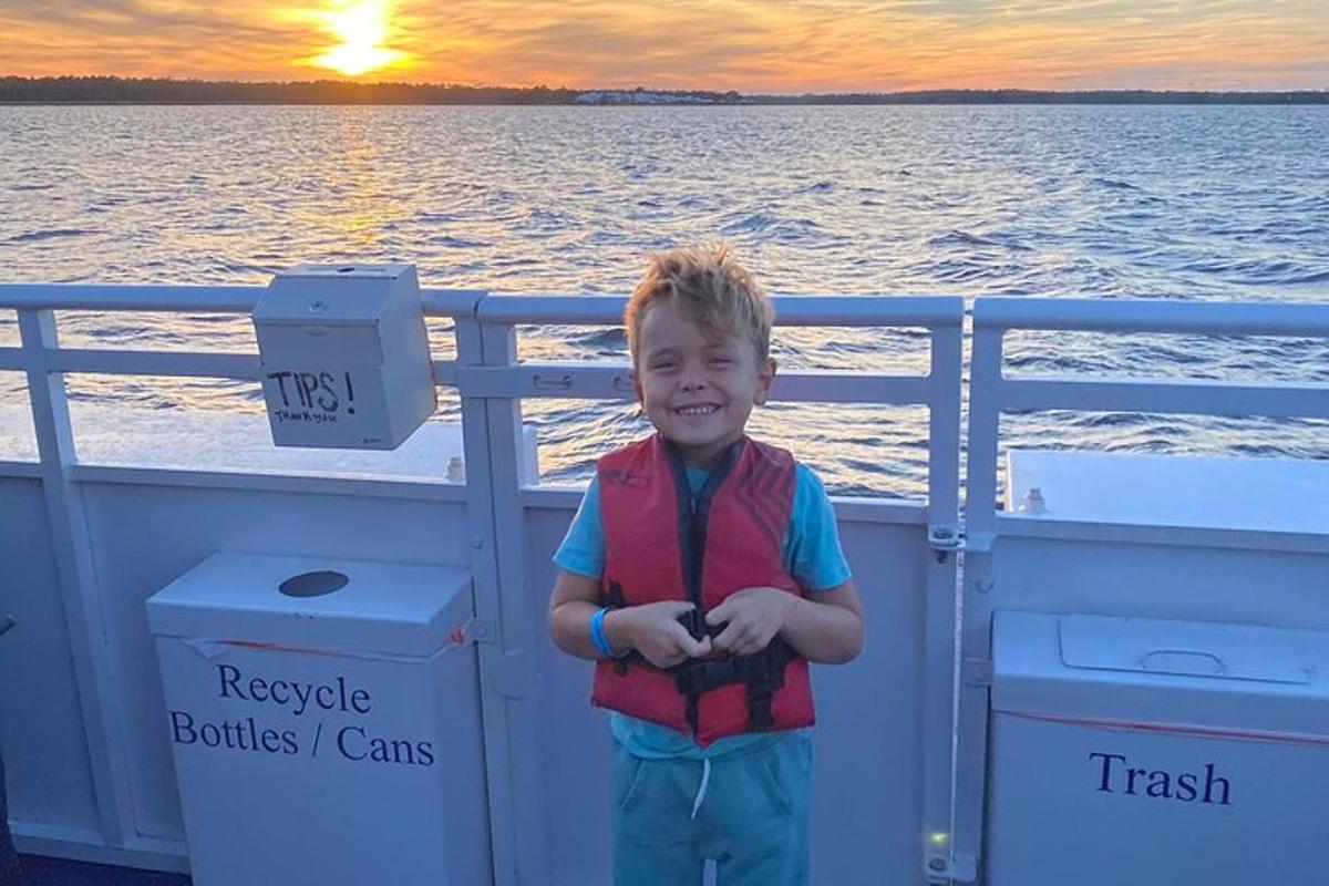 a young boy standing on a boat at sunset