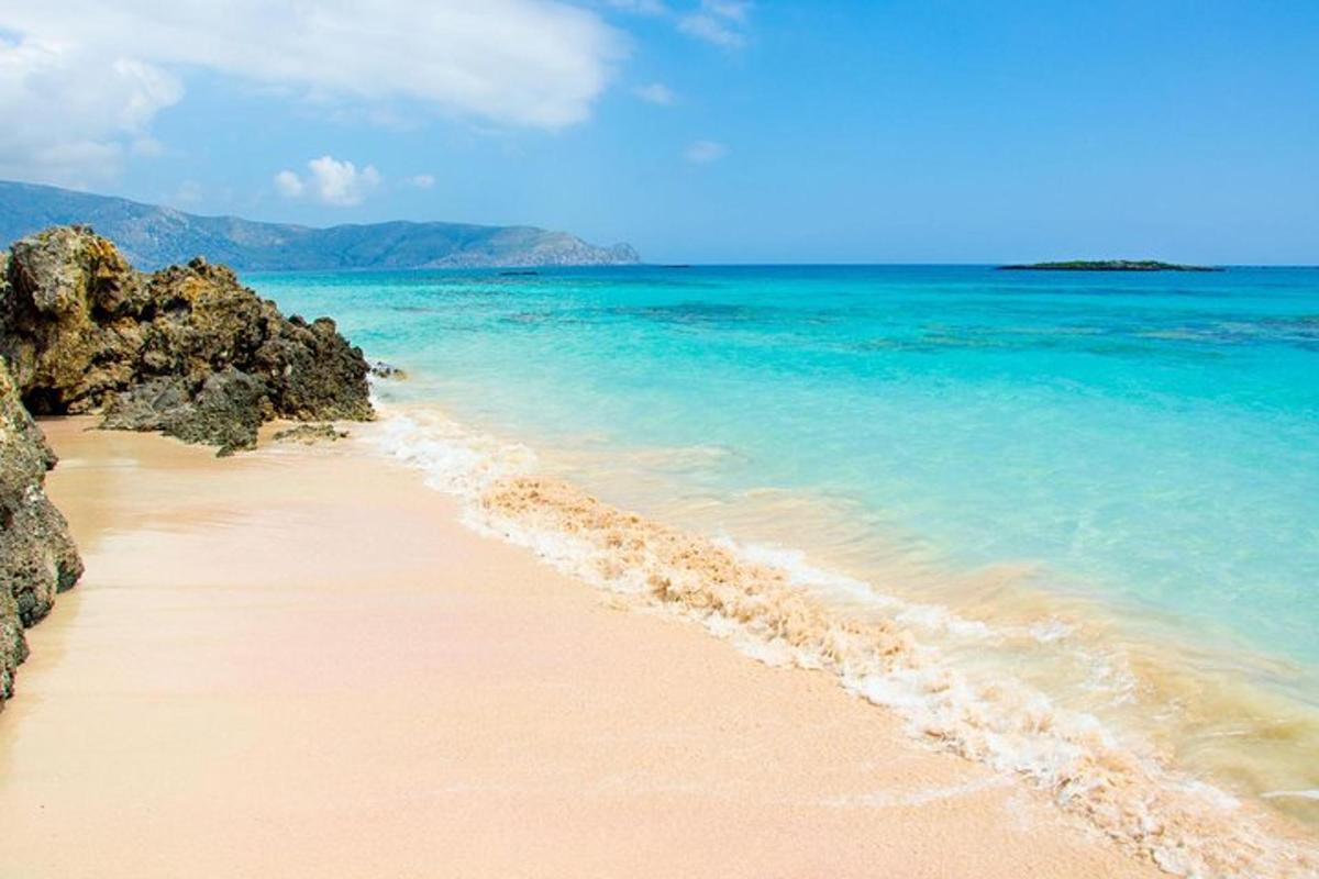 a sandy beach with blue water and rocks