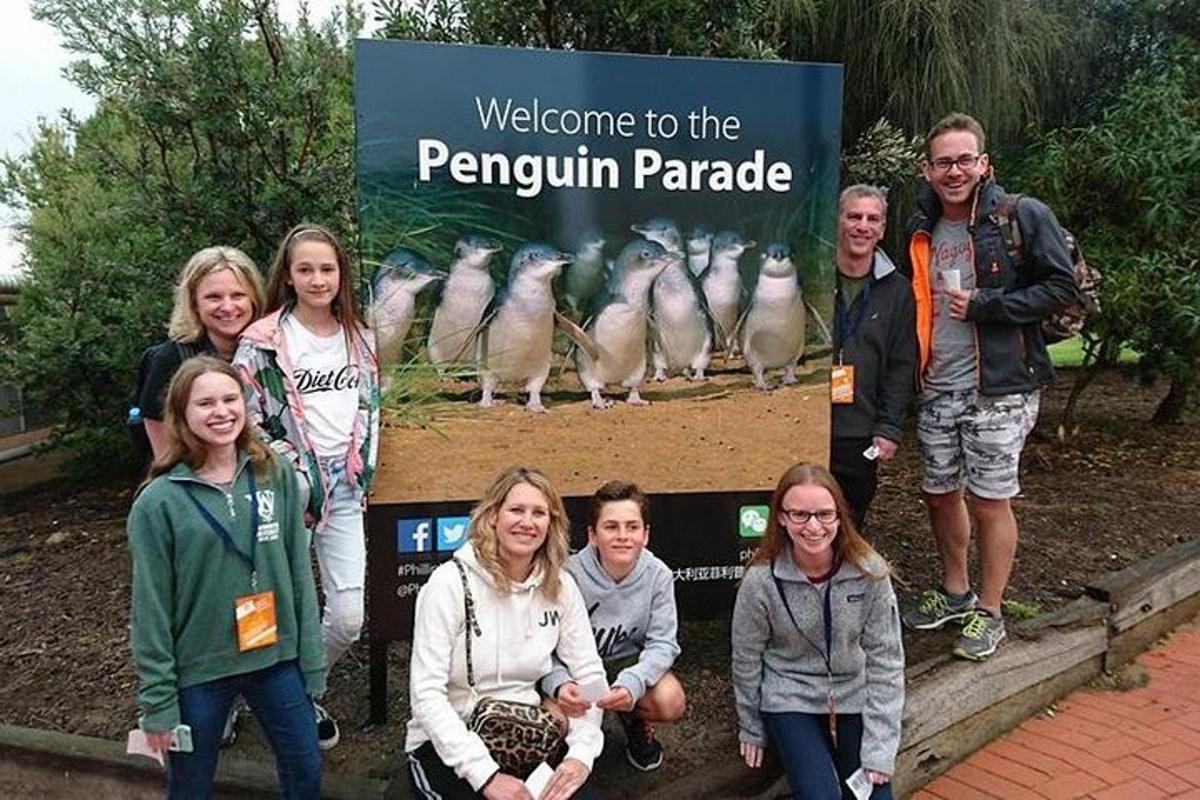 Un grupo de personas de pie frente a un desfile de pingüinos.