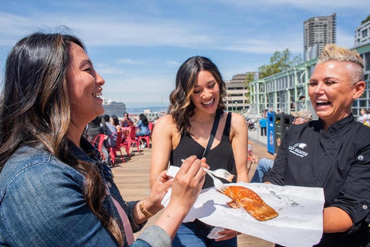 two women laughing while eating food on a boardwalk