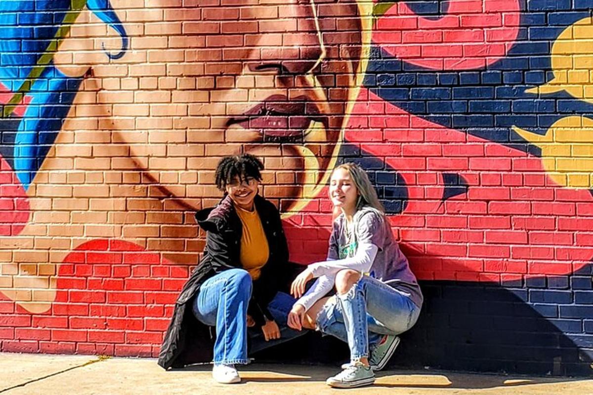 two women sitting in front of a wall with a mural