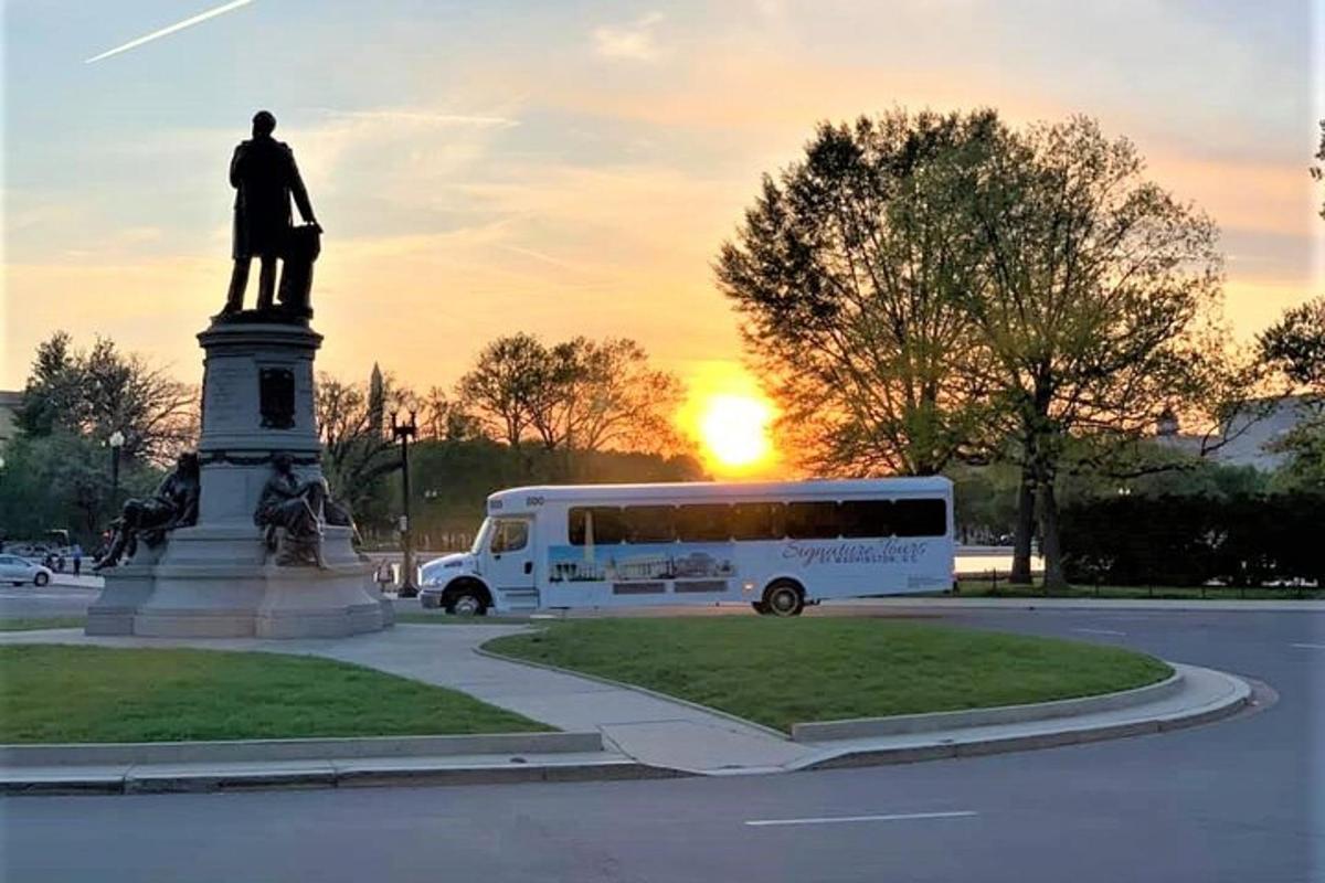 un autobús aparcat davant d'una estàtua amb la posta de sol