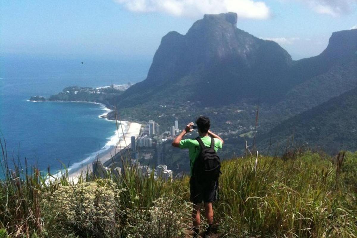 un home dret dalt d'un turó fent una foto de l'oceà