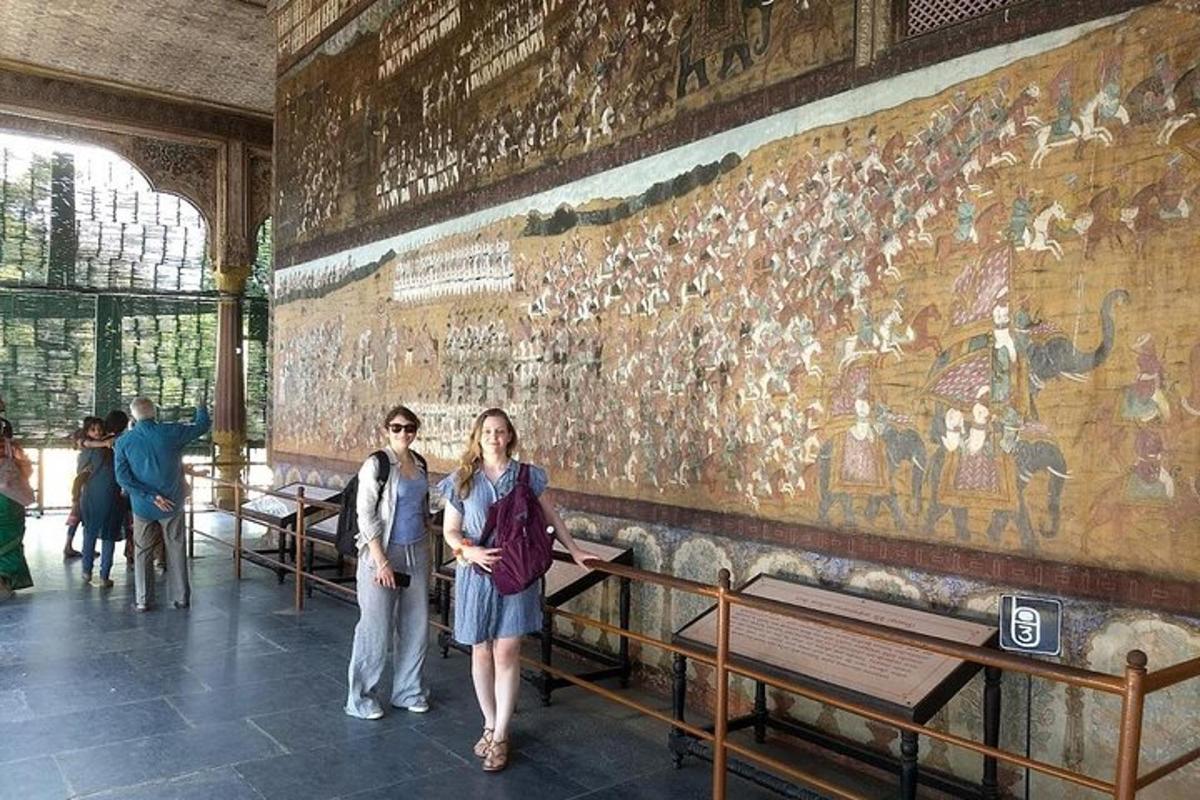 two women standing in front of a wall with a tapestry