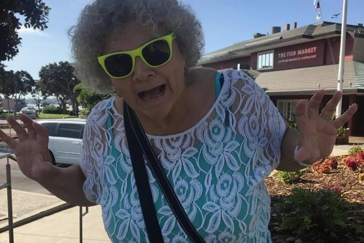 an older woman wearing sunglasses standing with her arms out