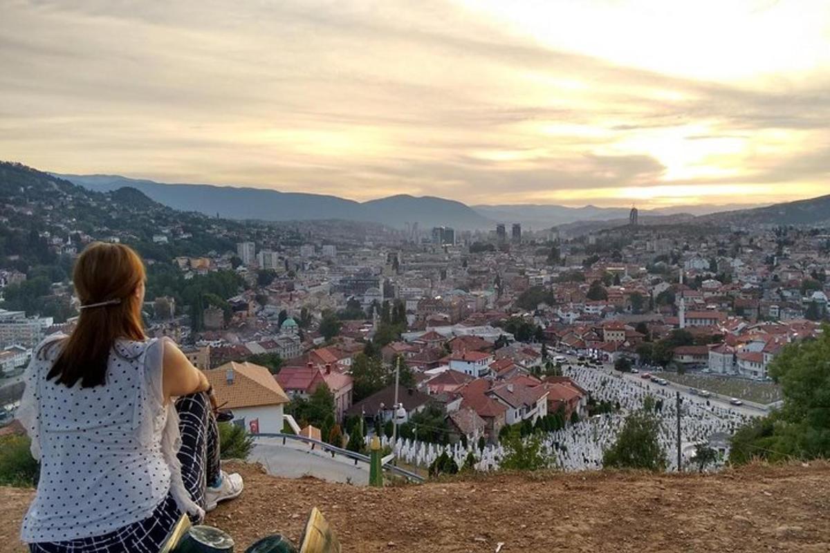 a woman sitting on a hill looking at a city