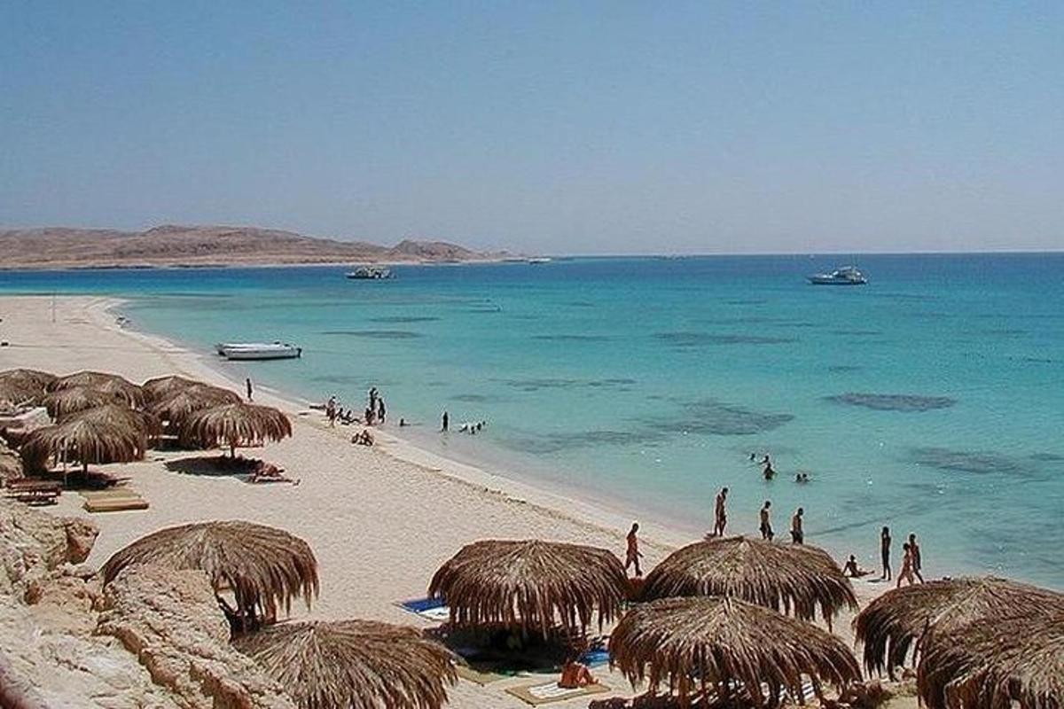Una playa con sombrillas de paja y gente en el agua.