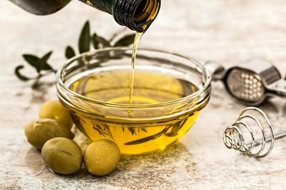 a bottle of olive oil being poured into a bowl of olives
