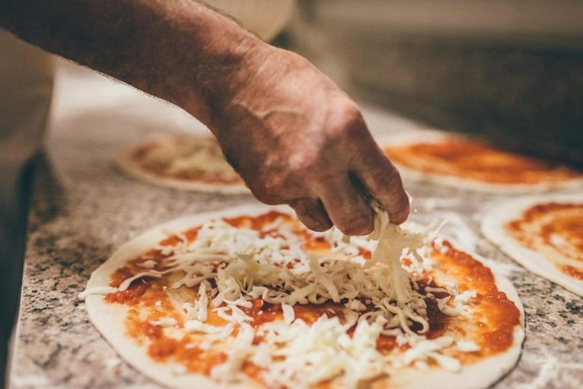 una persona espolvoreando queso encima de una pizza