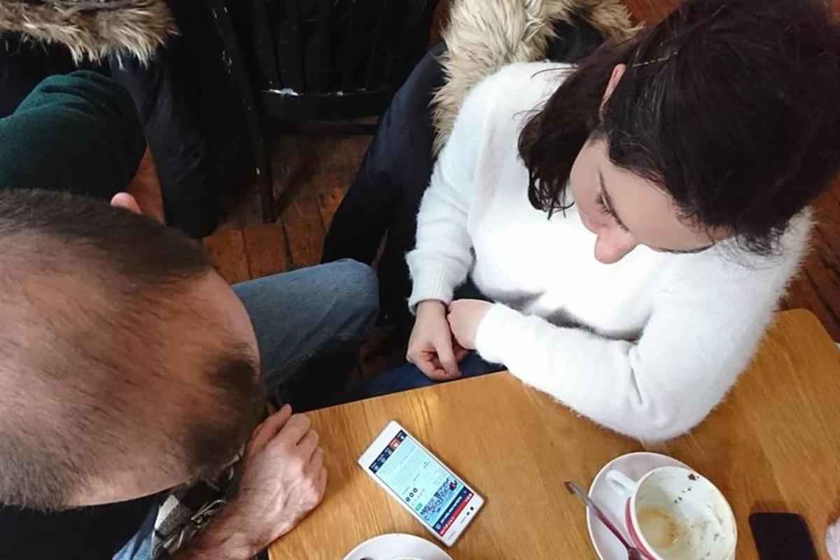 nainen istuu pöydässä kännykkä kädessään