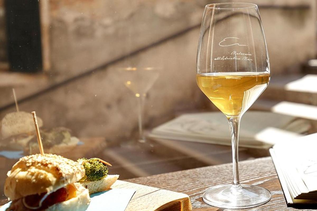 uma taça de vinho branco e um sanduíche em uma mesa